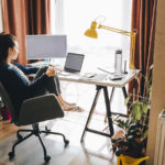 A photo of woman working on a computer at a desk in her home. work-from-home stocks