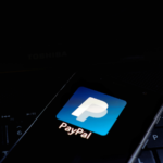 PayPal Holdings, Inc. (PYPL) icon displayed on smartphone with keyboard background. is an American multinational financial technology company operating an online payment
